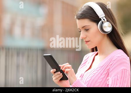 Un adolescent sérieux qui écoute de la musique avec un casque navigue sur son téléphone dans la rue Banque D'Images