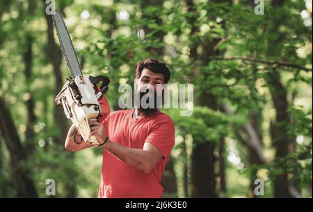 Thème de l'agriculture et de la foresterie. Bûcheron avec tronçonneuse sur fond de forêt. Jeune homme élégant qui se pose comme un bûcheron. Banque D'Images