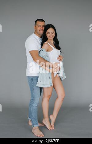 Un homme heureux encadre sa petite amie enceinte et regarde dans l'appareil photo. Un mari affectueux épouse en douceur la femme enceinte s'attendant à un bébé Banque D'Images