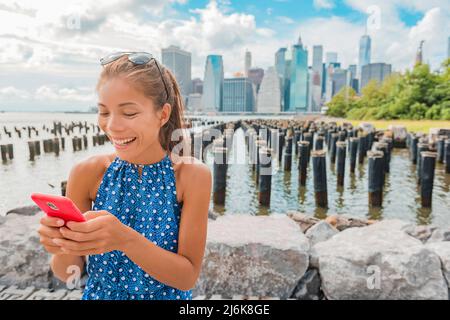 Une touriste de New York utilisant l'application sur le téléphone à côté de Manhattan City Skyline Waterfront. Les personnes qui marchent en profitant de la vue sur le centre-ville depuis le Brooklyn Bridge Park Banque D'Images