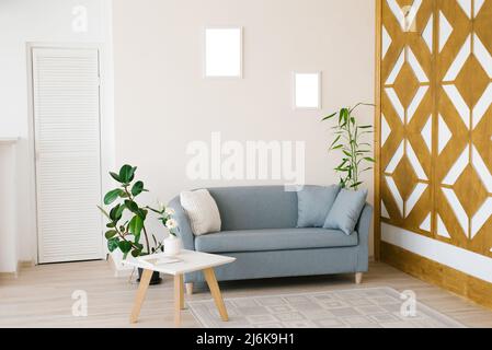 Un canapé bleu poussiéreux avec oreillers, une table basse blanche, des plantes en pot dans un salon lumineux et confortable. Cadres de maquette pour affiches sur le mur Banque D'Images