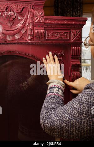 Femme mains accrochent bois sculpté ornements au carton en bois de couleur rouge clair avec verre rond en face dans maison de chalet en bois. Une nouvelle vie pour l'ancien Banque D'Images