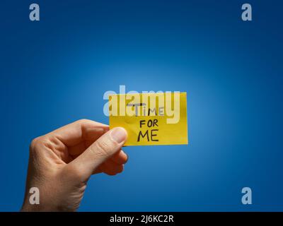 Une femme tenant un papier note jaune avec l'expression temps pour moi sur elle dans sa main sur un ciel bleu. Gros plan. Banque D'Images