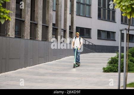 Livrez un garçon de plats à emporter sur un scooter électrique avec un capuchon jaune et une boîte isotherme pour aliments. Service de livraison express de nourriture depuis les cafés et les restaurants. Transporteur sur le scooter livrant la nourriture. Banque D'Images