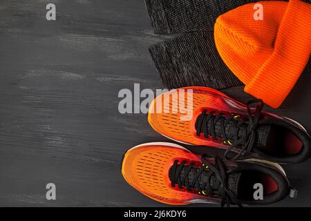 Baskets orange, bonnet tricoté orange, leggings de course chauds sur une table en bois sombre Banque D'Images