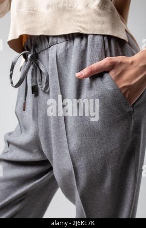 gros plan d'une jeune fille élégante dans un pantalon gris debout avec sa main dans sa poche contre un mur blanc Banque D'Images