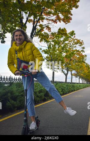 Une fille fait un scooter avec son pied sur le côté pour l'équilibre le long de la piste en perspective et rires Banque D'Images