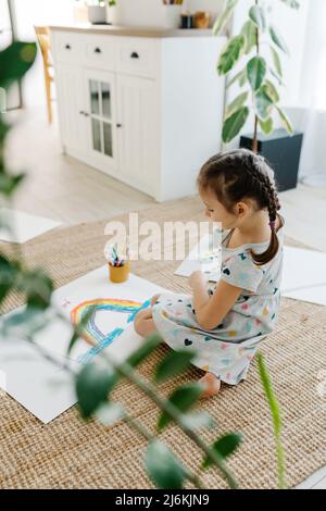 Enfant couché sur le sol et tient son dessin avec l'arc-en-ciel Banque D'Images