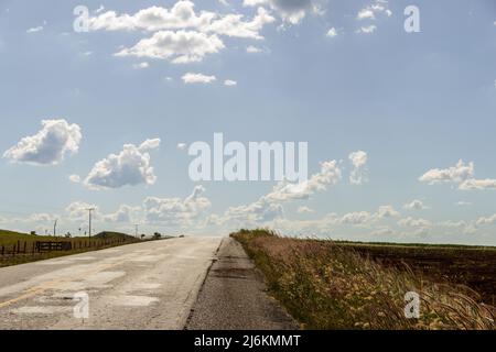 Goias, Brésil – 30 avril 2022 : détail d'une autoroute avec asphalte et beaucoup d'herbe et de ciel bleu avec quelques nuages. Banque D'Images