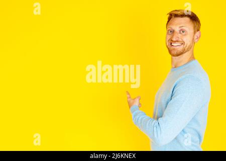 Jeune homme joyeux pointant vers l'arrière avec le doigt sur l'arrière-plan jaune de l'espace de copie Banque D'Images