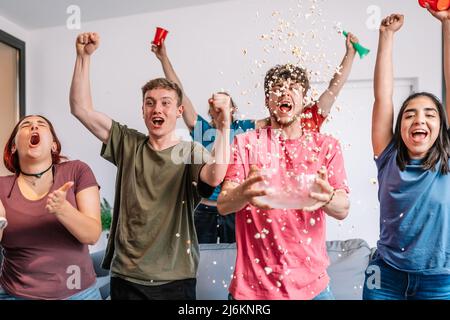 de jeunes amis lancent sans enthousiasme du pop-corn dans les airs après la victoire de leur équipe, diffusés à la télévision. Banque D'Images