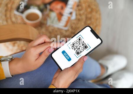 Femme tenant un smartphone avec code QR à l'écran à la maison, gros plan Banque D'Images