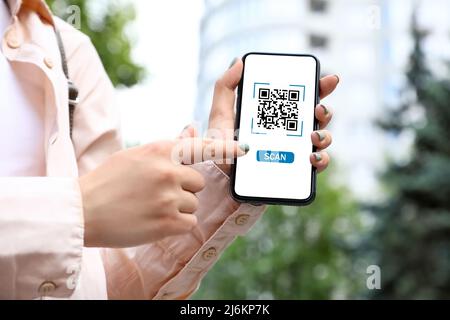 Femme tenant un smartphone avec code QR à l'écran en plein air, en gros plan Banque D'Images