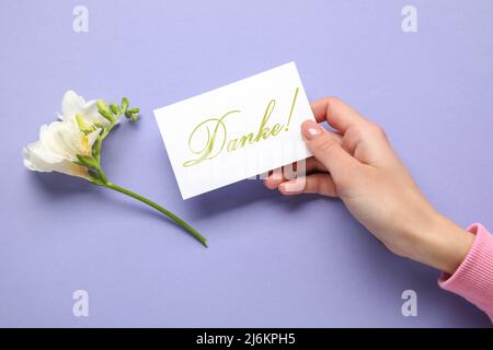 Carte de main femelle avec mot DANKE (allemand pour remerciement) et belle fleur sur fond lilas Banque D'Images