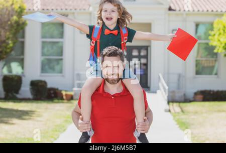 Un père et un fils étonnés courent avec le père après être revenus de l'école. École, famille, éducation et concept de plein air. Papa et fils s'amusent près de l'école Banque D'Images