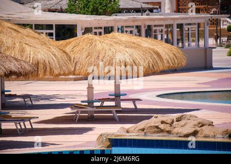 Des chaises longues vides sous des parasols en paille sur le côté de la piscine dans un complexe tropical. Vacances d'été et concept d'escapade Banque D'Images