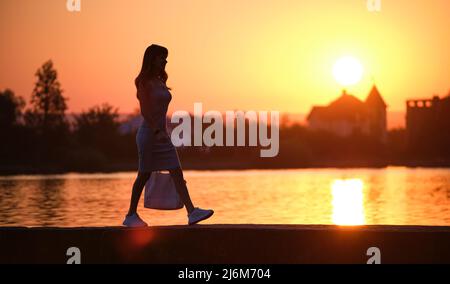 Femme solitaire piétonne marchant seule sur le bord du lac lors d'une soirée chaude. Concept de solitude et de relaxation Banque D'Images