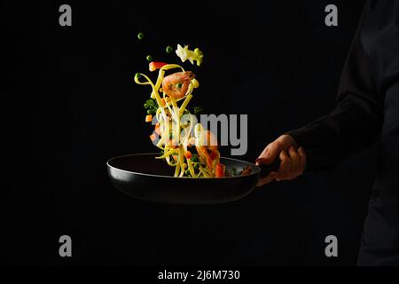 Le chef cuisite des fruits de mer avec des pâtes italiennes dans une poêle sur fond noir. Aliments surgelés en vol. Il y a de l'espace libre à insérer. Fruits de mer. Healt Banque D'Images