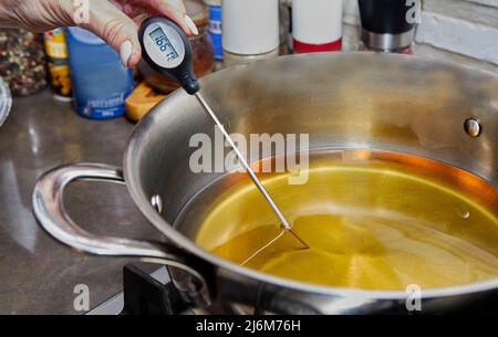 Chef vérifie la température de l'huile chauffée dans la cuve sur le poêle à gaz avec thermomètre. Banque D'Images