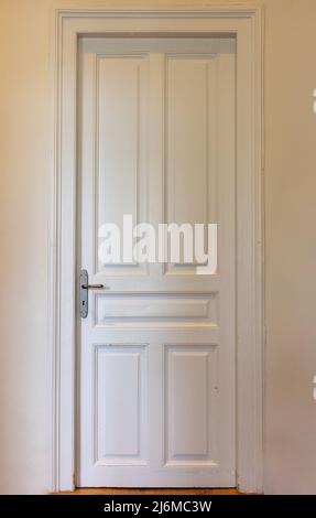 Grande porte intérieure en bois rétro. Porte blanche classe avec bouton et serrure à clé, vue avant. Porte fermée sur le fond du mur de la maison. Banque D'Images