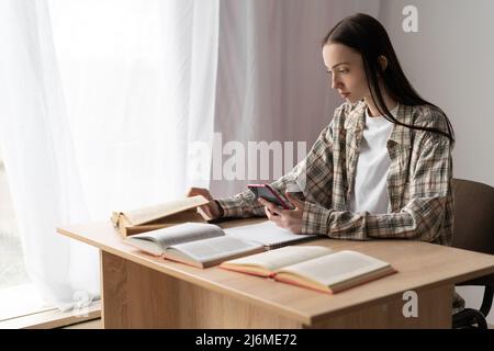 jeune étudiante étudiant étudiant à distance en utilisant un smartphone moderne, enseignement à distance en ligne à la maison, technologie pour l'e-learning, vue de profil Banque D'Images