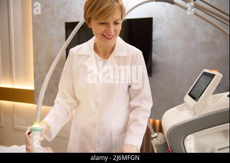 Charmante femme blonde de race blanche, médecin esthéticienne en salle de cosmétologie matérielle donnant des procédures de soins du corps au patient dans la clinique de spa de bien-être Banque D'Images