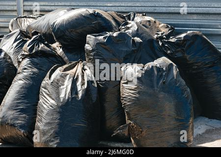 De nombreux grands sacs noirs de déchets se tiennent dehors dans les ordures. Nettoyage du territoire. Faisons du monde plus propre. Arrière-plan. Banque D'Images