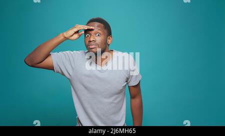 Personne confuse utilisant la main sur le front pour regarder autour, à la recherche de l'indice dans la distance. Jeune adulte regardant vers l'avant, ayant intérêt à l'exploration et se sentant pensif, homme confiant avec curiosité. Banque D'Images