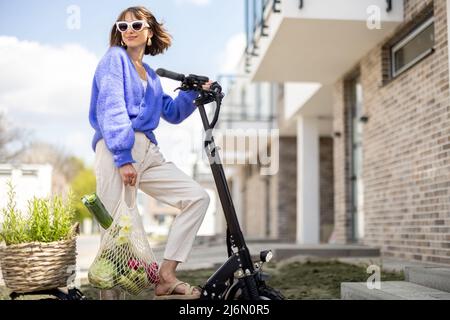 Femme qui rentre à la maison avec des légumes frais sur un scooter électrique Banque D'Images