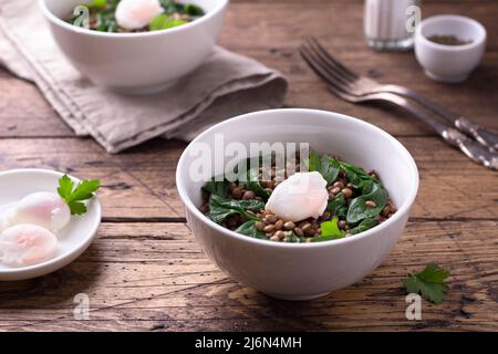 Lentilles bouillies aux épinards, aux herbes, aux épices et aux œufs pochés dans des bols en céramique sur fond de bois. Simple nourriture saine maison Banque D'Images