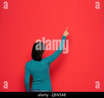Vue arrière d'une femme pointant vers quelque chose sur un mur rouge Banque D'Images