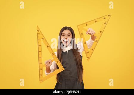 un enfant heureux tient une règle de triangle mathématique à l'école sur fond jaune, l'éducation Banque D'Images