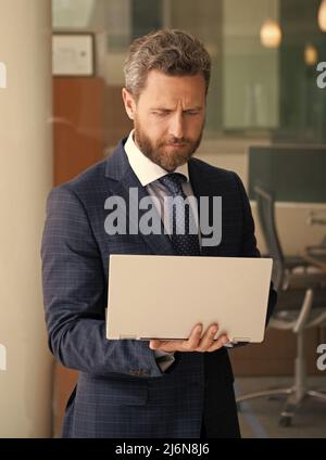 un homme d'affaires mature et concentré travaille en ligne sur un ordinateur moderne en dehors du bureau, une entreprise agile. Banque D'Images