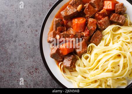 Bouchées lentement de bœuf épicé au vin rouge avec des légumes servis avec des nouilles en gros plan dans une assiette sur la table. Vue horizontale du dessus Banque D'Images