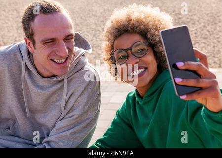 jeune femme latine et homme caucasien souriant tout en prenant une photo de selfie avec le téléphone mobile, concept de style de vie et d'amitié Banque D'Images