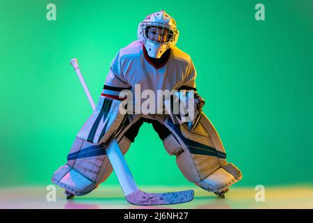 Portrait complet d'un garçon, joueur de hockey, entraînement de gardien de but, jouant isolé sur fond vert dans la lumière du néon Banque D'Images