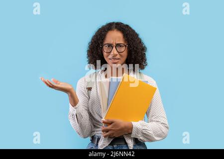 Femme noire frustrée étudiant avec sac à dos et ordinateurs portables se sentant stressé sur fond bleu studio Banque D'Images