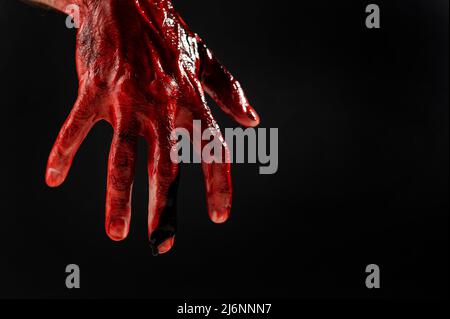 Gros plan d'une main masculine colorée de sang sur fond noir. Banque D'Images