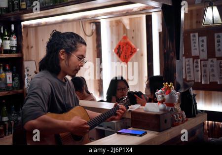 XIAMEN, le 3 mai 2022 (Xinhua) -- Wang Shengfen joue de la guitare à sa 'cantine de nuit' à Xiamen, dans la province de Fujian du sud-est de la Chine, le 1 mai 2022. Wang Shengfen, 37 ans, et Chen Wayne, 24 ans, de Kaohsiung et Taichung, respectivement, de Taïwan, dans le sud-est de la Chine, se livrent tous deux à des activités de restauration à Xiamen. Wang dirige une « cantine nocturne » et Chen ouvre un restaurant familial avec son père. En 2016, Wang Shengfen et son père sont venus sur le continent pour chercher des opportunités d'affaires. Bientôt, il a ouvert un restaurant avec des amis dans le district de Jimei de Xiamen. En 2022, il a commencé sa propre b Banque D'Images