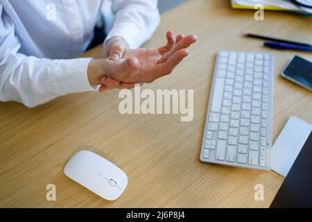 Vue rapprochée de la femme d'affaires qui tient la main et qui ressent une douleur au poignet en utilisant la souris et le clavier de l'ordinateur pendant longtemps Banque D'Images