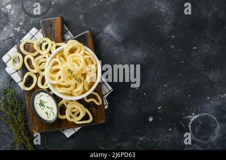 Rondelles d'oignon. Restauration rapide. Croustilles d'oignon croustillantes dans un bol noir en céramique avec sauce à la crème aigre et oignons dans un support en bois sur fond de béton noir ancien. AM Banque D'Images