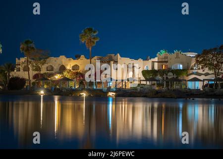 Les bâtiments, les chaises longues et les parasols se reflètent dans l'eau de mer calme de la plage la nuit dans la station balnéaire de Charm El Sheikh, en Égypte Banque D'Images