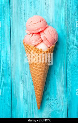 Crème glacée à la framboise dans un cornet de gaufres sur fond bleu. Banque D'Images