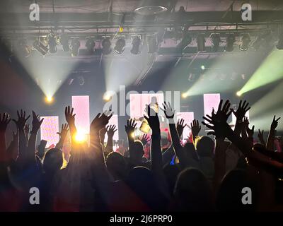 Un public excité à un concert avec les lumières clignotantes et les bras et les mains soulevées dans l'air Banque D'Images