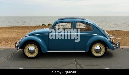 Classic Blue VW Beetle garée sur la promenade du front de mer avec la mer et la plage en arrière-plan. Banque D'Images