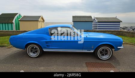 Classic Blue Ford Mustang GTA garé sur avec des cabanes de plage de bord de mer et l'océan en arrière-plan. Banque D'Images