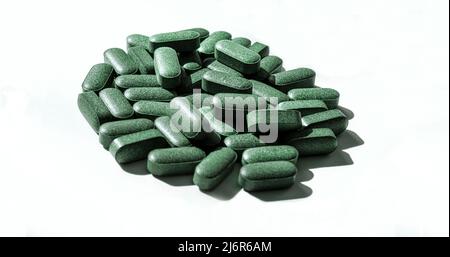 Pilules de chlorella, spiruline, herbe d'orge sur fond blanc avec ombres sombres gros plan supplément nutritionnel, désintoxication superalimentaire soins de santé Banque D'Images