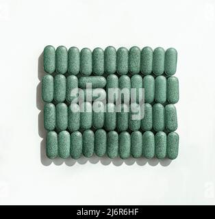 Chlorella, spiruline ou herbe d'orge dans les rangées en forme de pilule et deux pilules sur fond blanc supplément nutritionnel, désox superfood soins de santé Banque D'Images