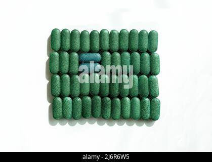 Chlorella, spiruline ou herbe d'orge dans les rangées en forme de pilule et deux pilules bleues sur fond blanc supplément nutritionnel, désetox santé superalimentaire Banque D'Images
