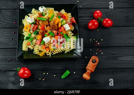 Pâtes Penne aux légumes, petits pois, poivrons, tomates, sauce, mozzarella sur fond de bois noir. Pâtes italiennes avec légumes et sp Banque D'Images